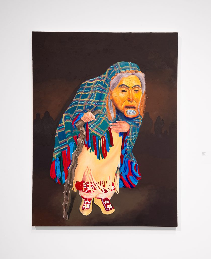 Painting of a figure hunched over a gnarled walking stick, wearing a mask with a large iridescent labret inlay and dark eyebrows. Grey hair and a wood-bark braid are visible. They are wearing a teal plaid fringed blanket over the head, a tan fringed skirt, and matching tan pants and shoes with white flowers on a red background. 