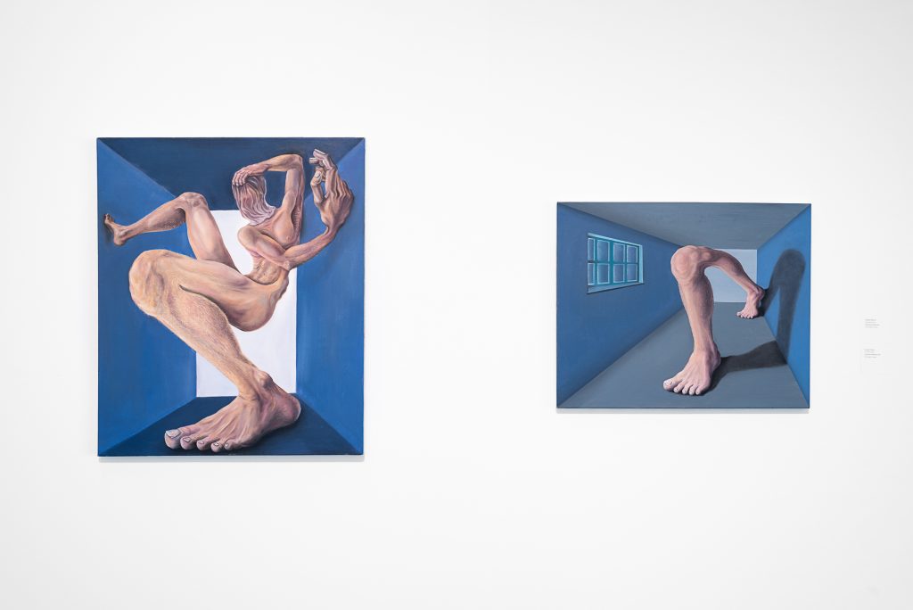 Two wall-mounted portraits of exaggerated, fleshy human figures seemingly trapped in a small blue room. The left image shows a full figure, the right shows a pair of legs joined at the knee. 