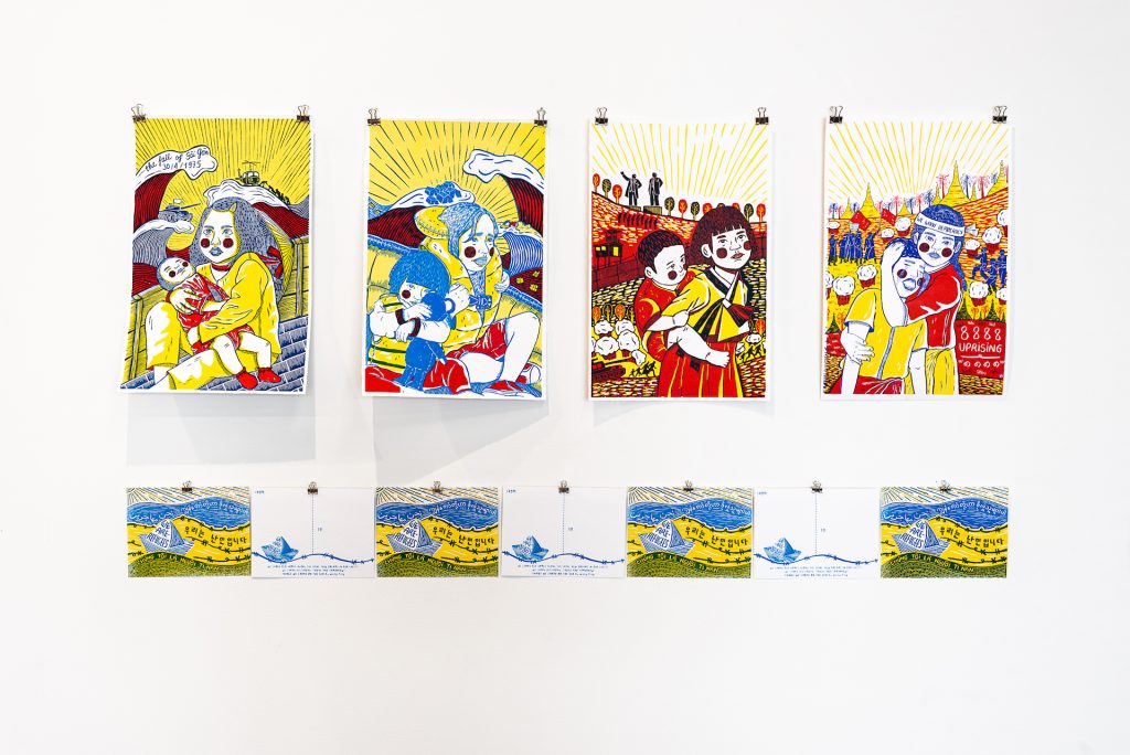 Wall-mounted posters in shades of bright yellow, blue, and red depicting female figures holding children amid refugee crises in Asia. Top row, left to right: Vietnam, in a boat with the text “the fall of Sai Gon 30/4/1975”; Syria, in a boat wearing life jackets; North Korea, walking along a field with statues in the background; Burma, amid a protest with the text “8888 uprising” and “We want democracy.” Bottom row: eight identical postcards of a boat, with the text “we are refugees”. 