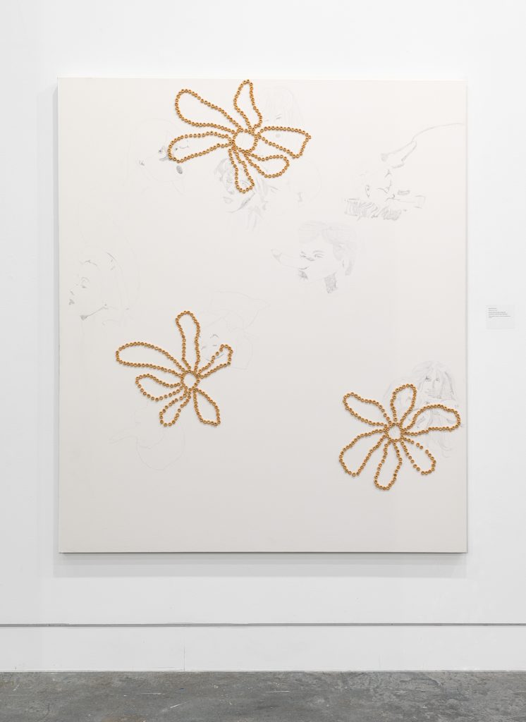 Cheerios cereal pieces are arranged into asymmetrical outlines of three flowers on a mostly-empty white canvas. Faint graphite sketches of faces are visible in the background. 