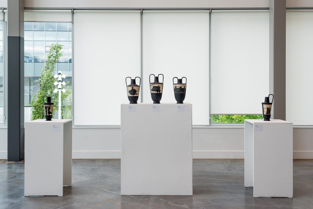 Five black ceramic vessels on plinths, with etchings that reveal tan-coloured clay below the paint. Each etching depicts different human figure on a couch. The three centre vessels share a large plinth and have two handles, the others have one handle and sit on smaller plinths. 