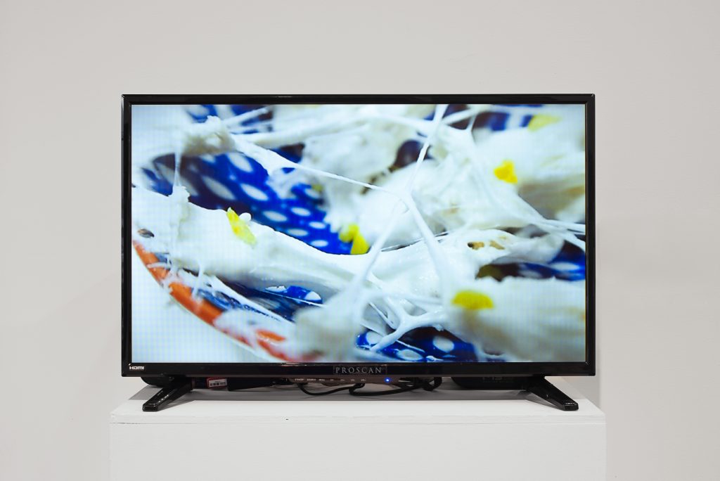 TV mounted on a plinth showing a closeup view of strands of melted marshmallows on a polka-dotted blue plate. 