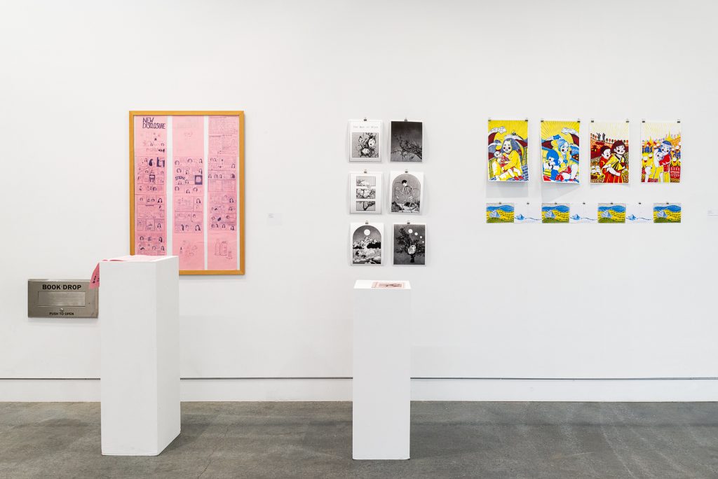 Three installations of works on paper. On the left, a pink zine lays open on a plinth with pages pages displayed in a wood frame on the wall behind. In the middle, a pale pink zine sits on a plinth with 6 black-and-white prints displayed on the wall behind. On the right are 4 bright yellow, blue and red prints, below is a series of eight blue and yellow postcards. 