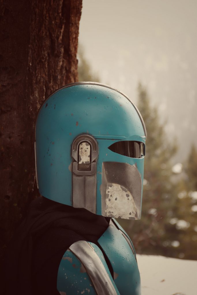 Side view of person wearing a teal and silver helmet, with snowy trees in the background. 
